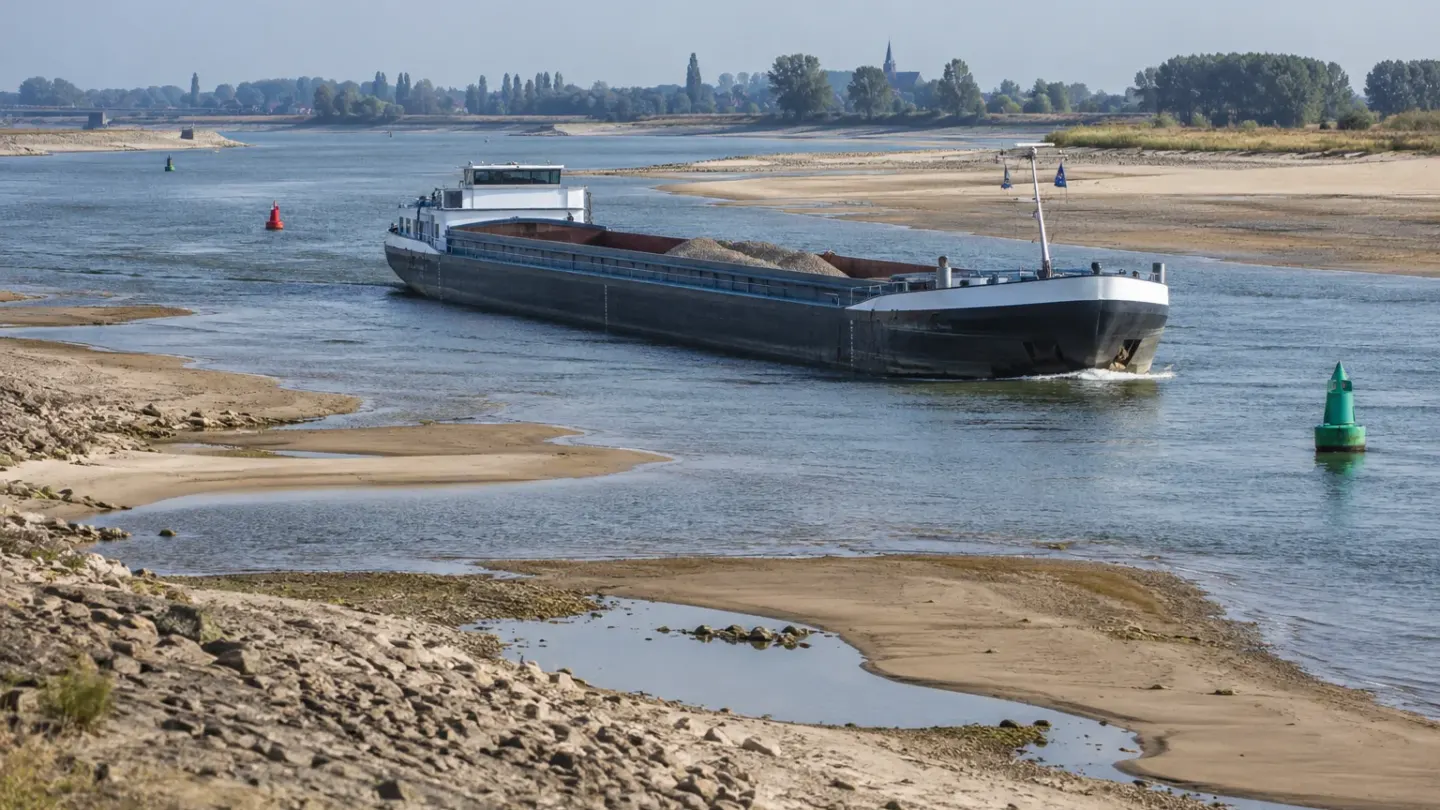 Binnenvaartschip vaart door een smalle geul tussen drooggevallen zandbanken