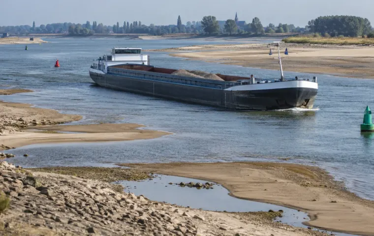 Binnenvaartschip vaart door een smalle geul tussen drooggevallen zandbanken