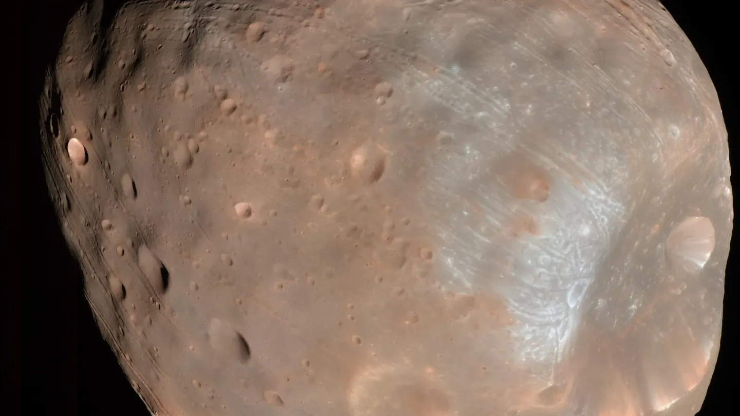 Kleurenopname van de onregelmatige, met kraters bedekte Marsmaan Phobos tegen een zwarte achtergrond.