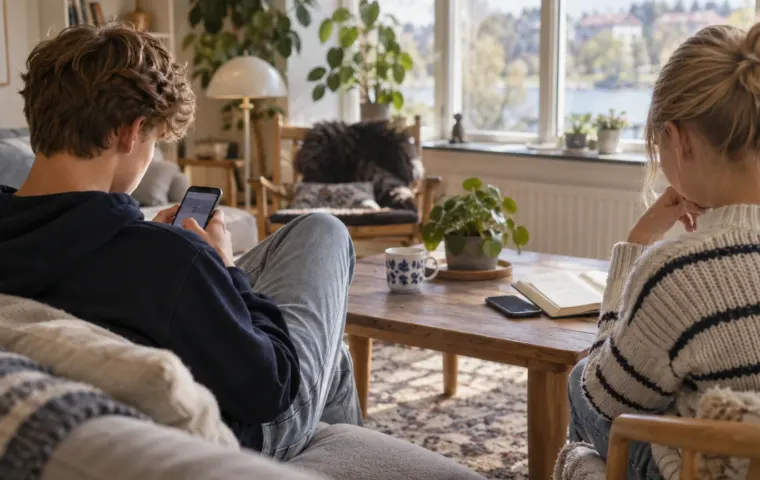 Twee jongeren zitten in een woonkamer; de een kijkt op een telefoon, de ander zit naast een boek en een weggelegde telefoon.